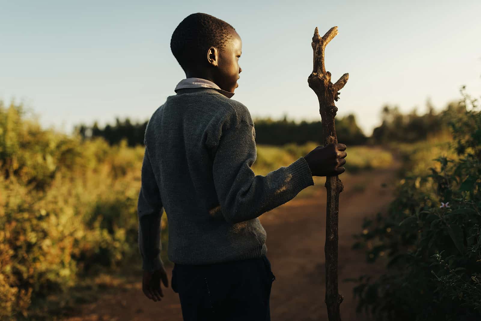 Kenyan boy walking a path with a walking stick