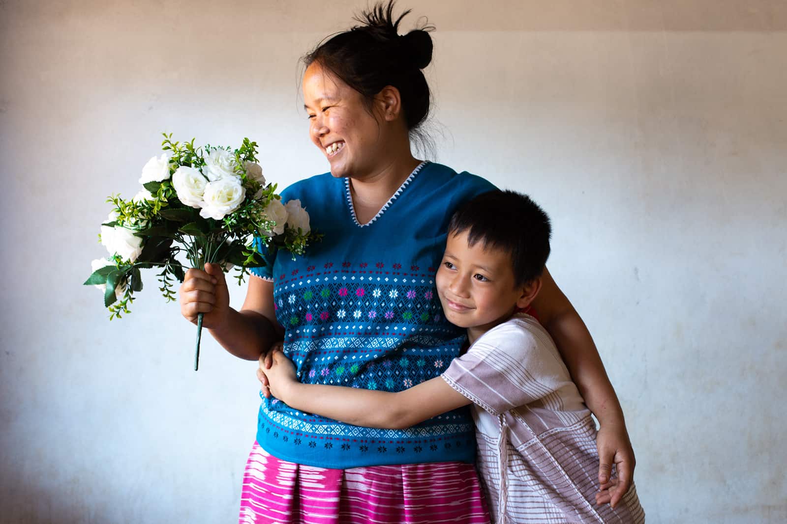 Mother holding flowers with child hugging her