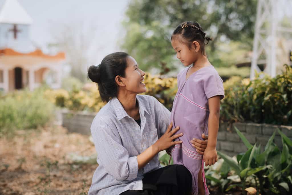 A happy newly sponsored child and her mother outside a Compassion project