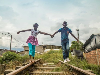 Two children holding hand walking along railroad tracks