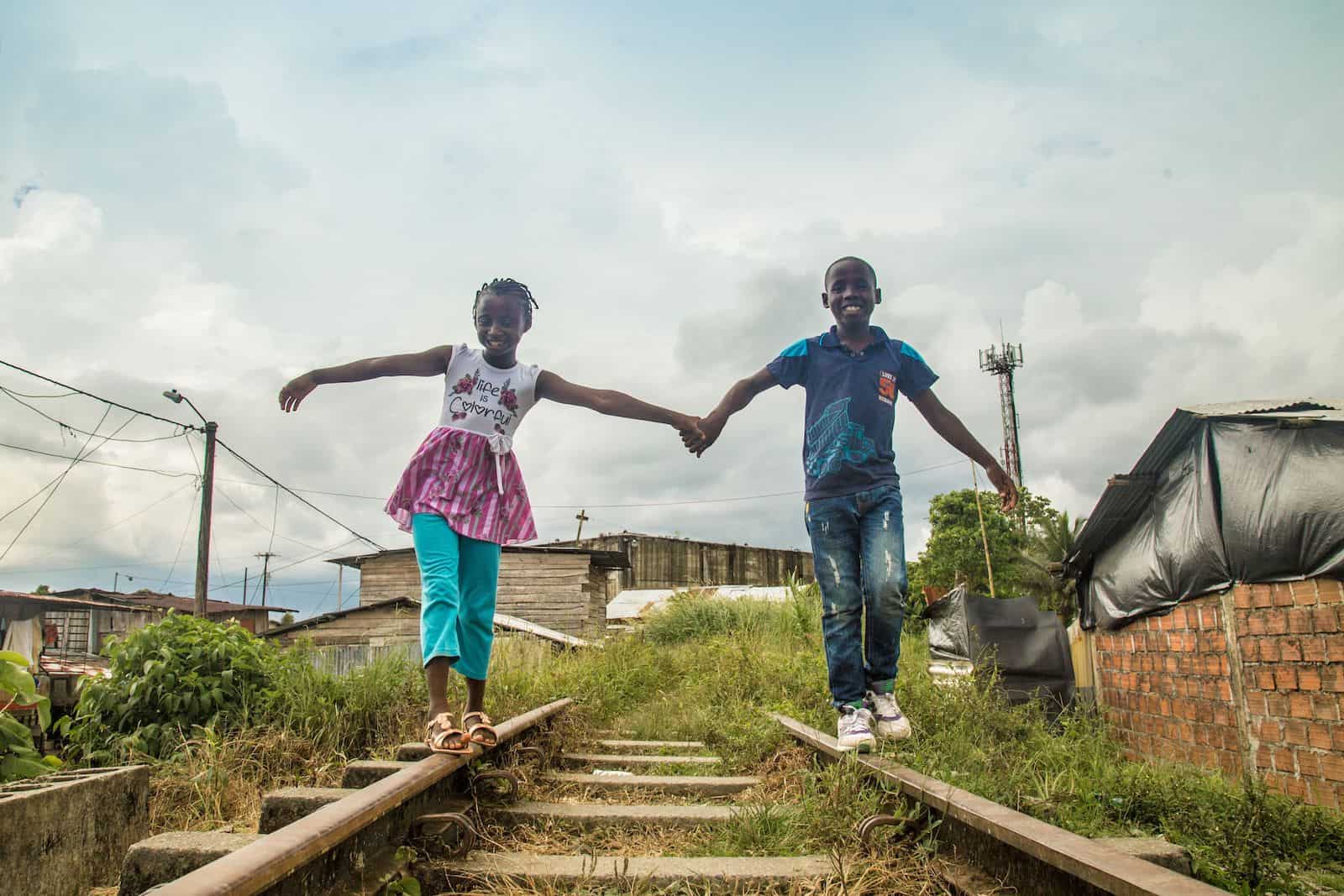 Two children holding hand walking along railroad tracks