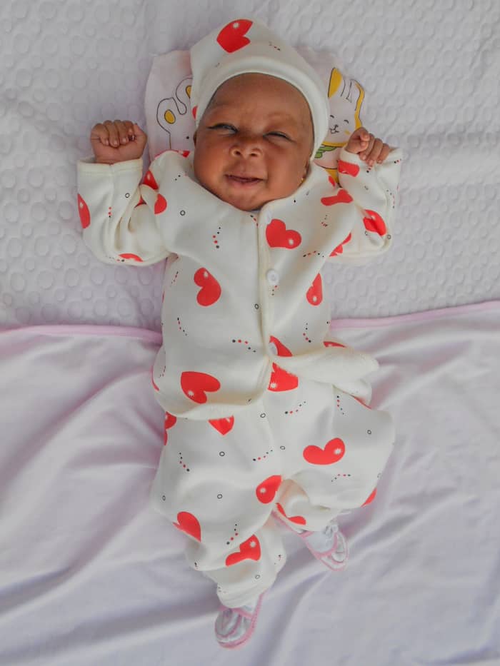 A baby on a blanket in a white and red outfit