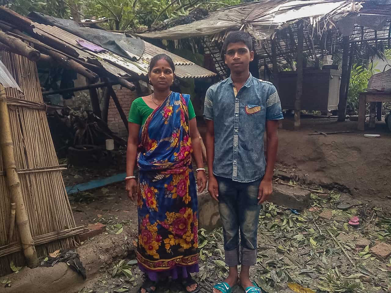 A boy and woman stand in front of a home damaged by Cyclone Amphan