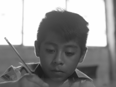 A boy holds a pencil, writing a letter.