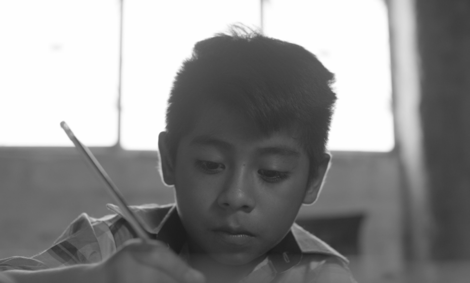 A boy holds a pencil, writing a letter.