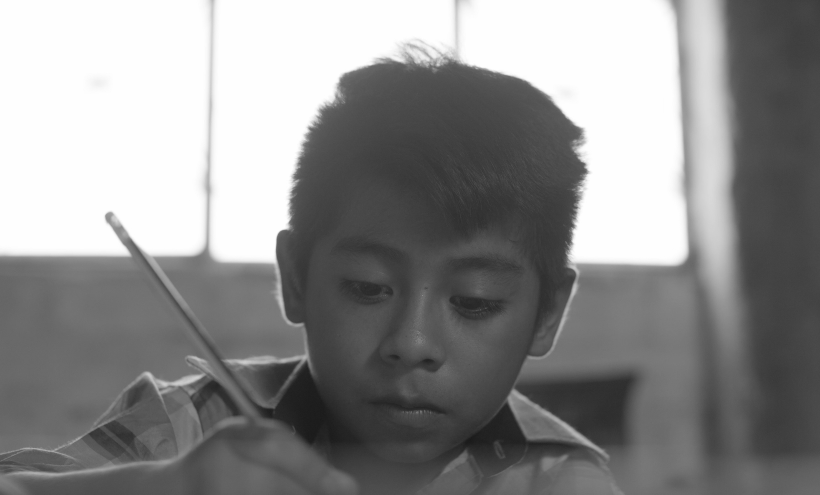 A boy holds a pencil, writing a letter.