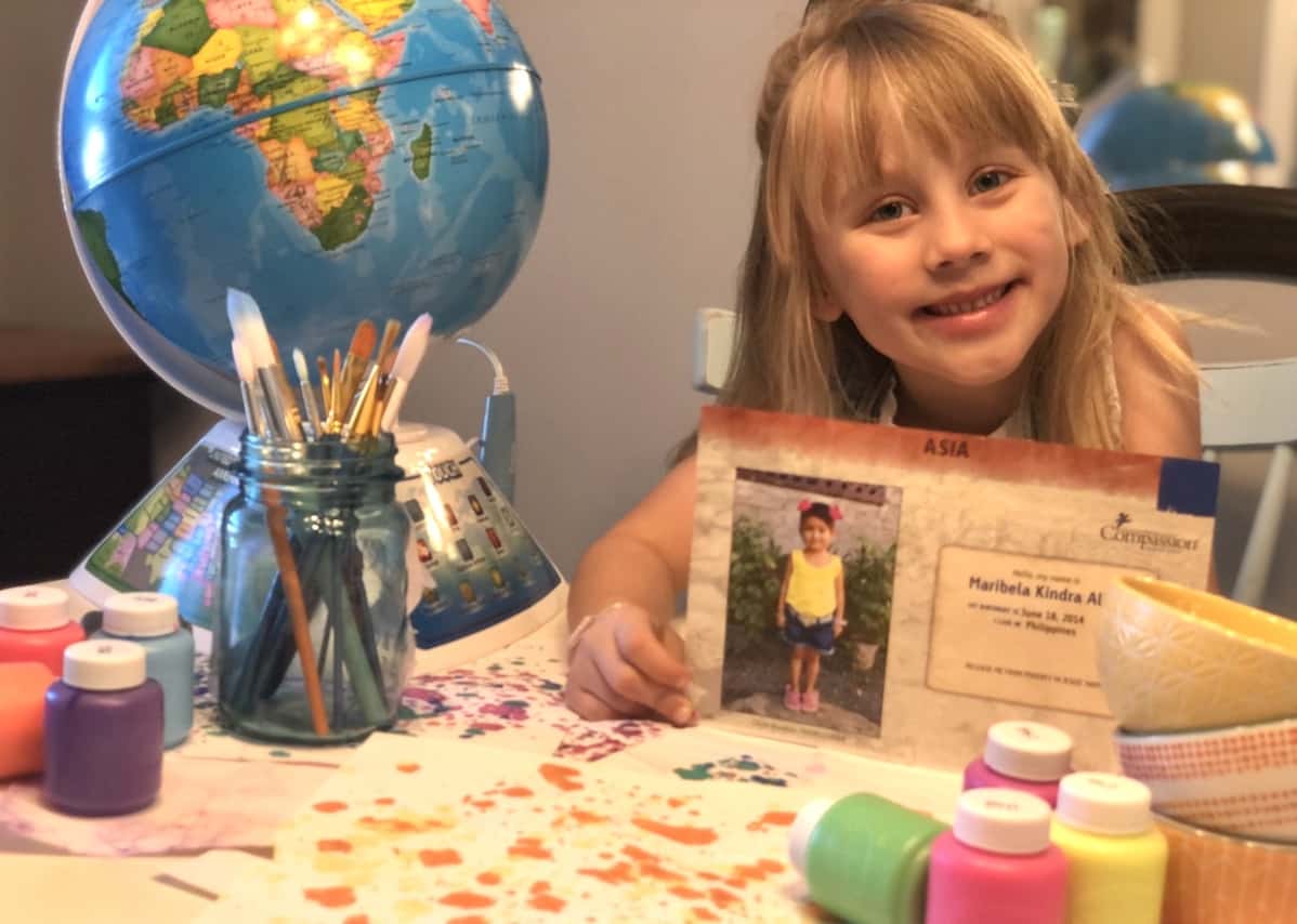 A girl sits by a globe, holding a picture of a girl