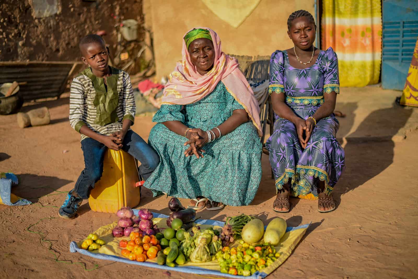 Three people sit in front of a blanket covered in vegetables.