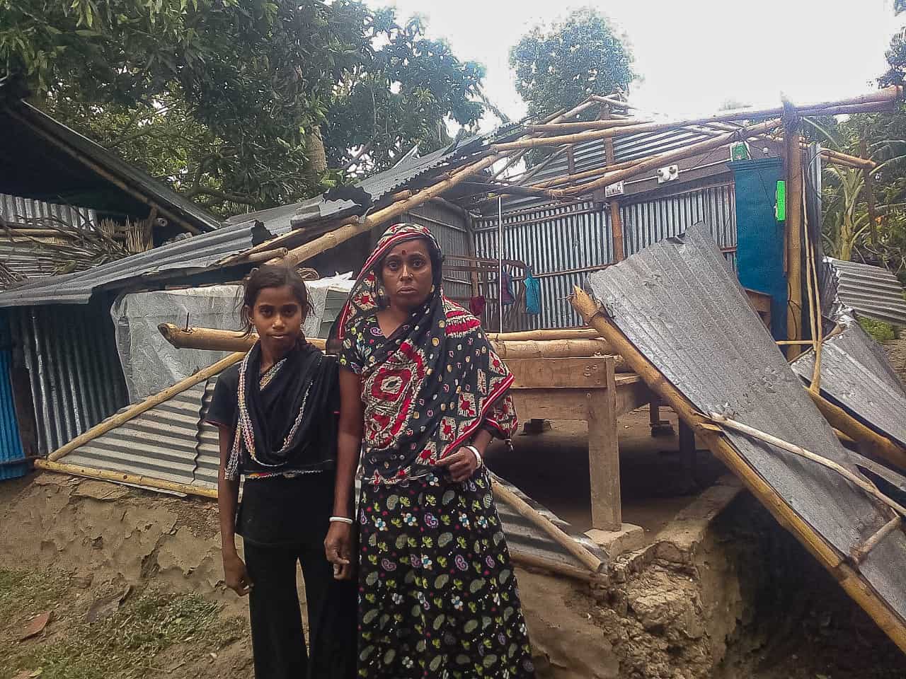A girl and woman stand in front of a damaged home.