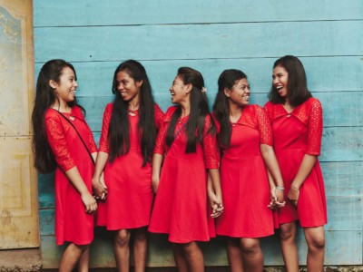 Five girls wear red dresses, laughing and standing in front of a green wall