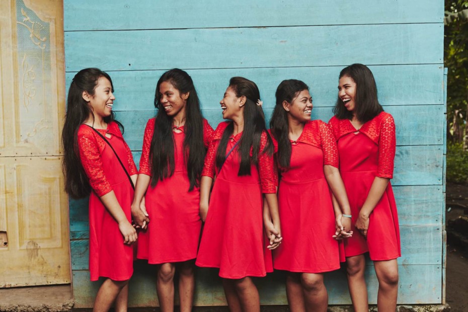 Five girls wear red dresses, laughing and standing in front of a green wall