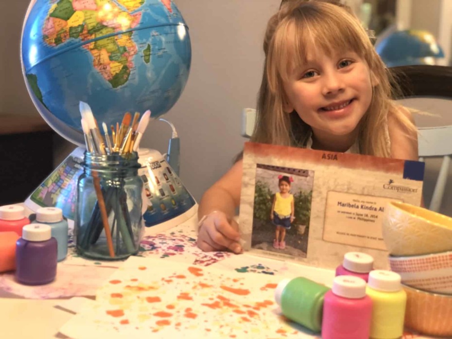 A girl sits by a globe, holding a picture of a girl