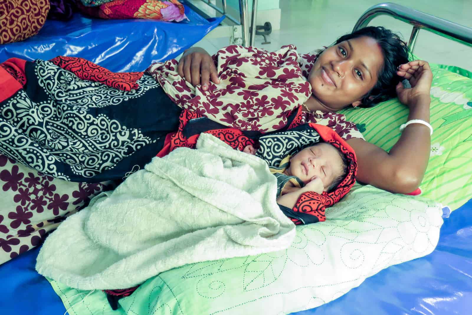 A mom and her baby lie in a hospital bed.