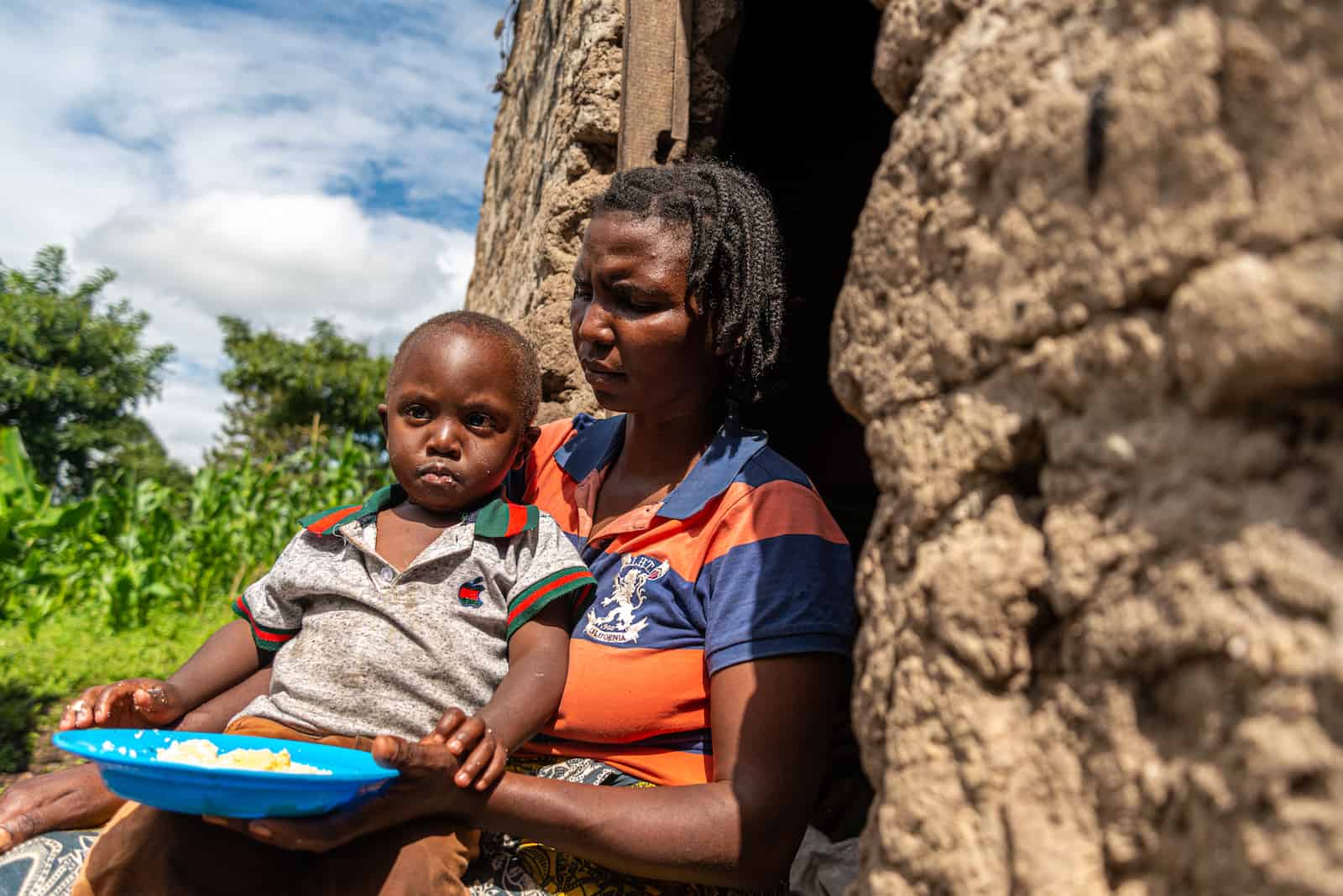 A woman holds a child with a bowl of food