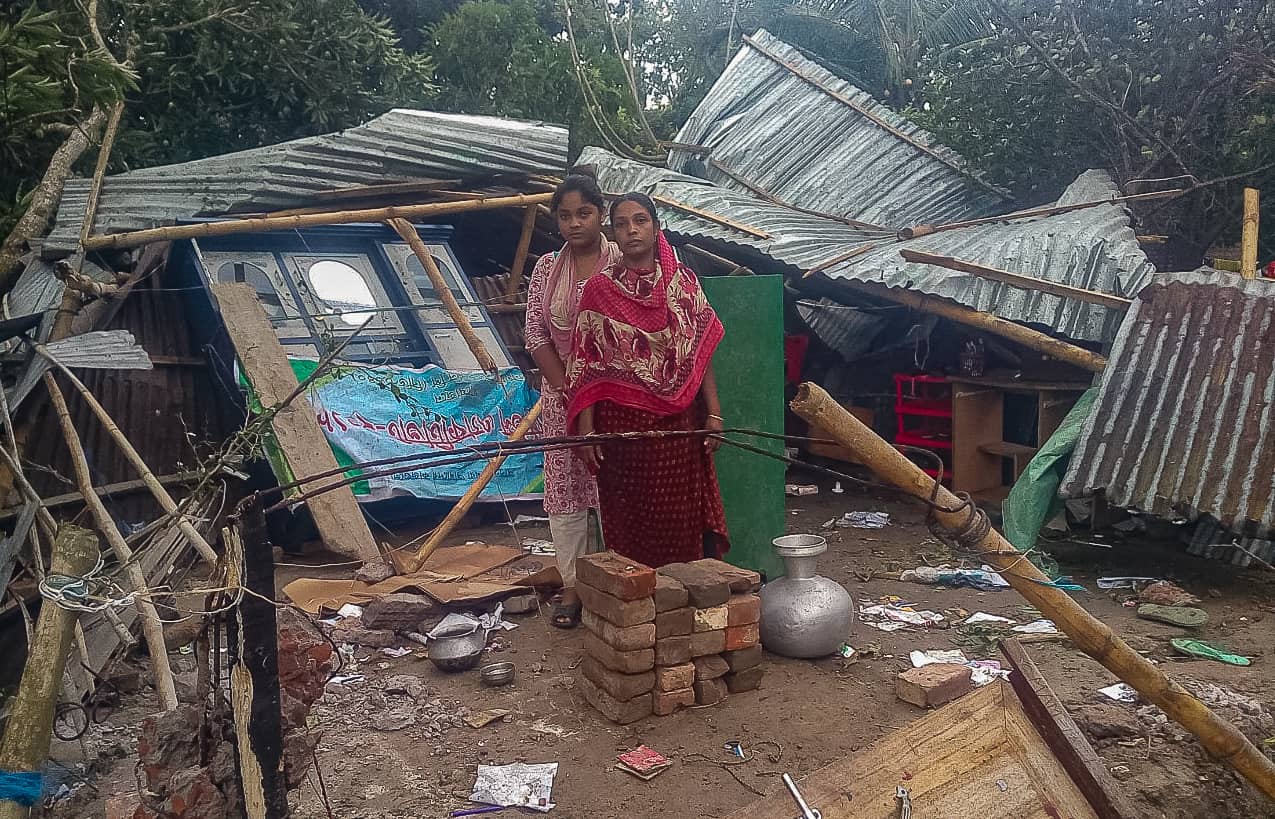 A girl and a woman stand in front of a home destroyed by Cyclone Amphan.