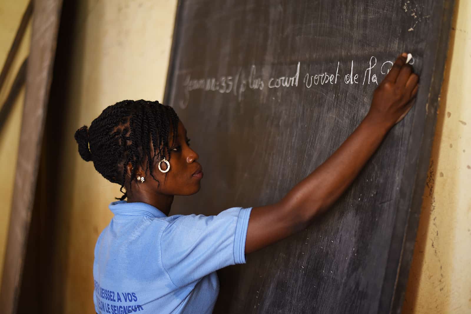 Carine wearing a blue shirt writing on a chalkboard