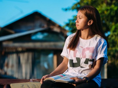 girl in a white shirt sitting outside with a book open on her lap