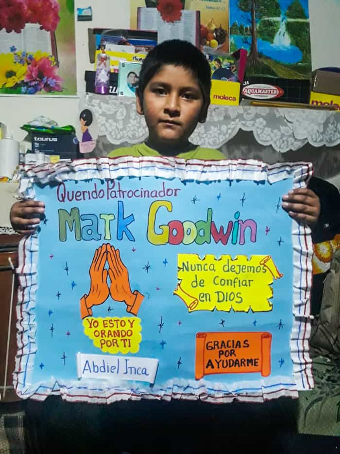 A boy holds a poster with praying hands on it and Spanish words.