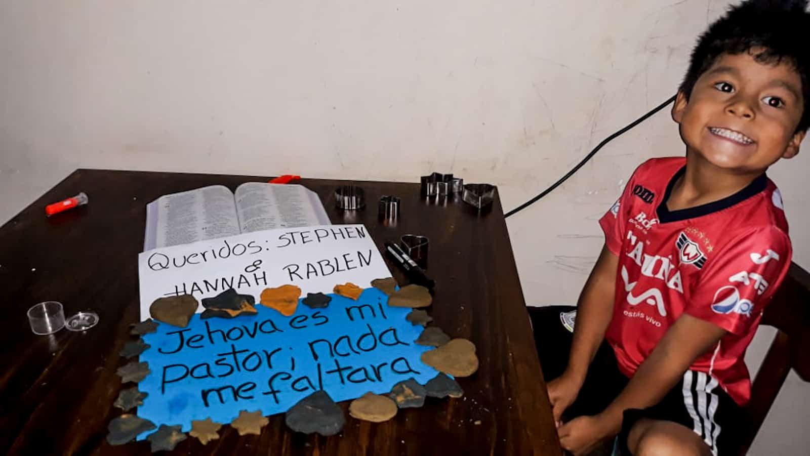 A boy sits by a table with a sign in Spanish