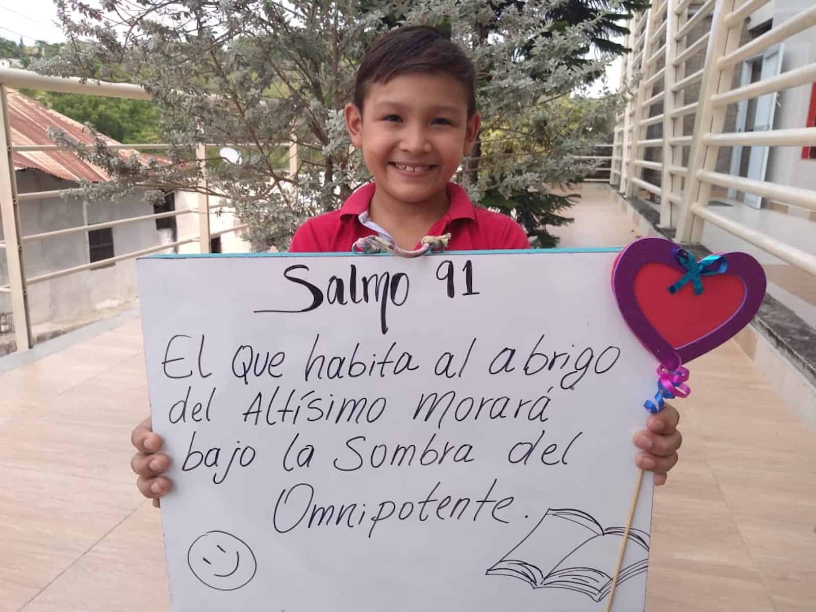 A boy holds a poster with a Bible verse written on it in Spanish.