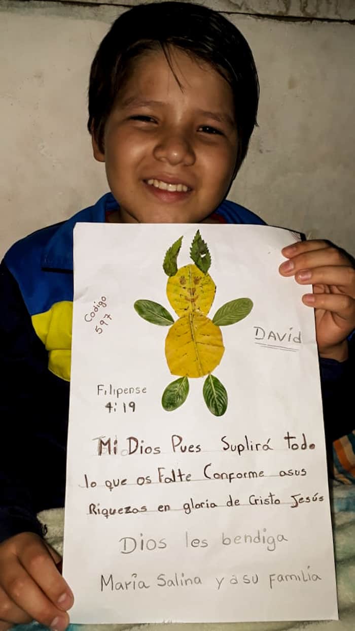 A boy holds a sign with an animal made out of leaves on it and Spanish writing.