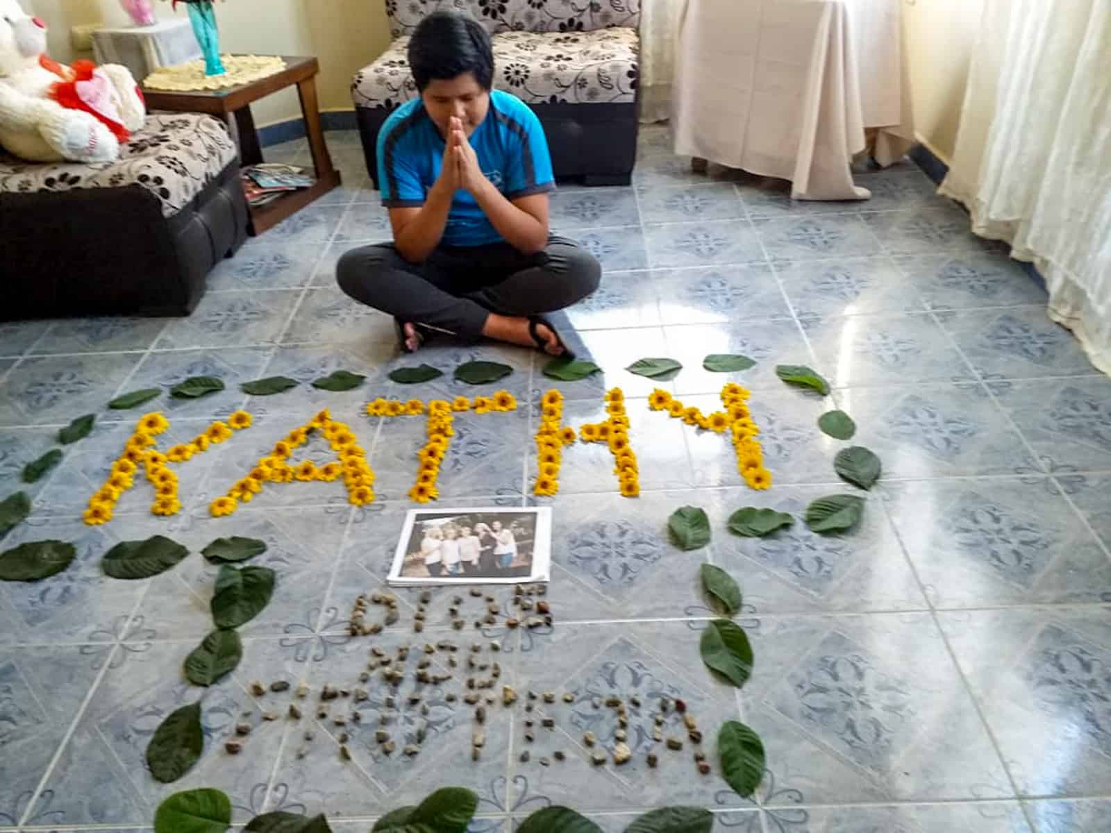 A boy sits in front of a collage made from flowers