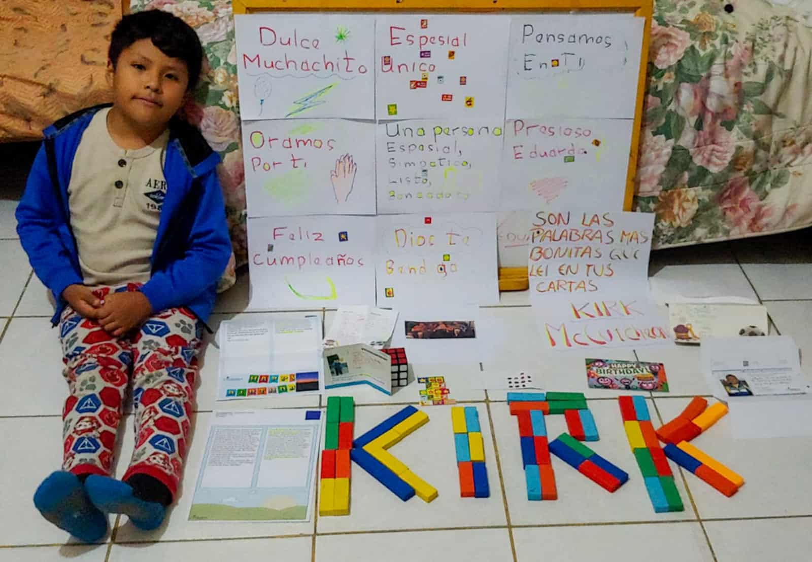 A boy sits next to posters written in Spanish