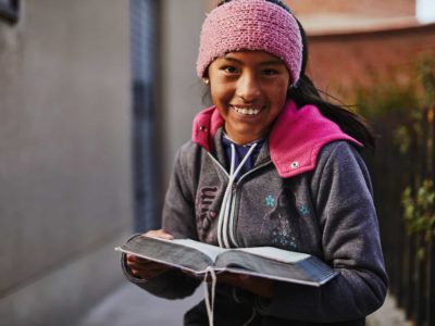 A girl in a pink hat holds a Bible.