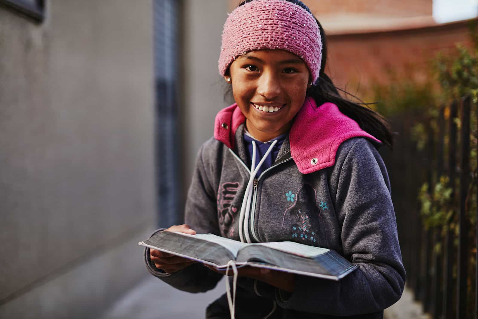 A girl in a pink hat holds a Bible.