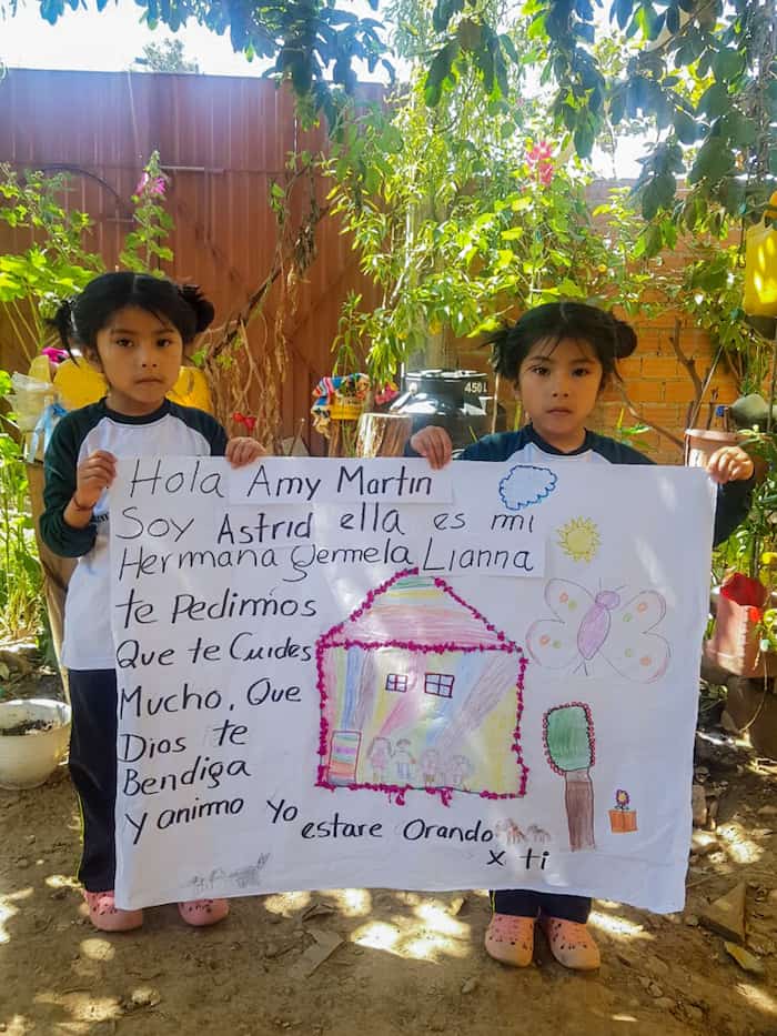 Twin girls hold up a poster with Spanish written on it.