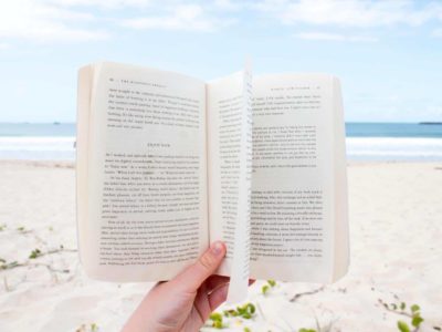 A hand holds a book on a beach