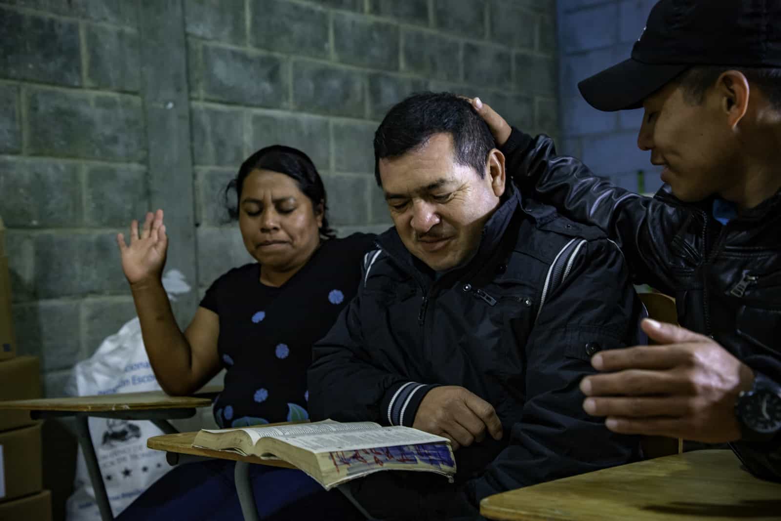 Three people sit together, praying.