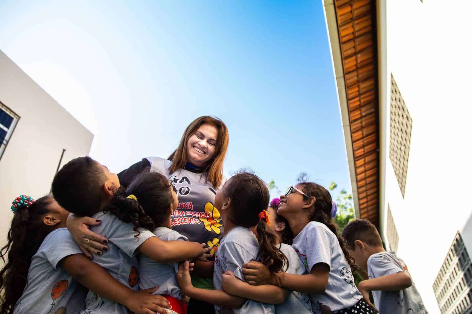 A woman is surrounded by children, hugging her.