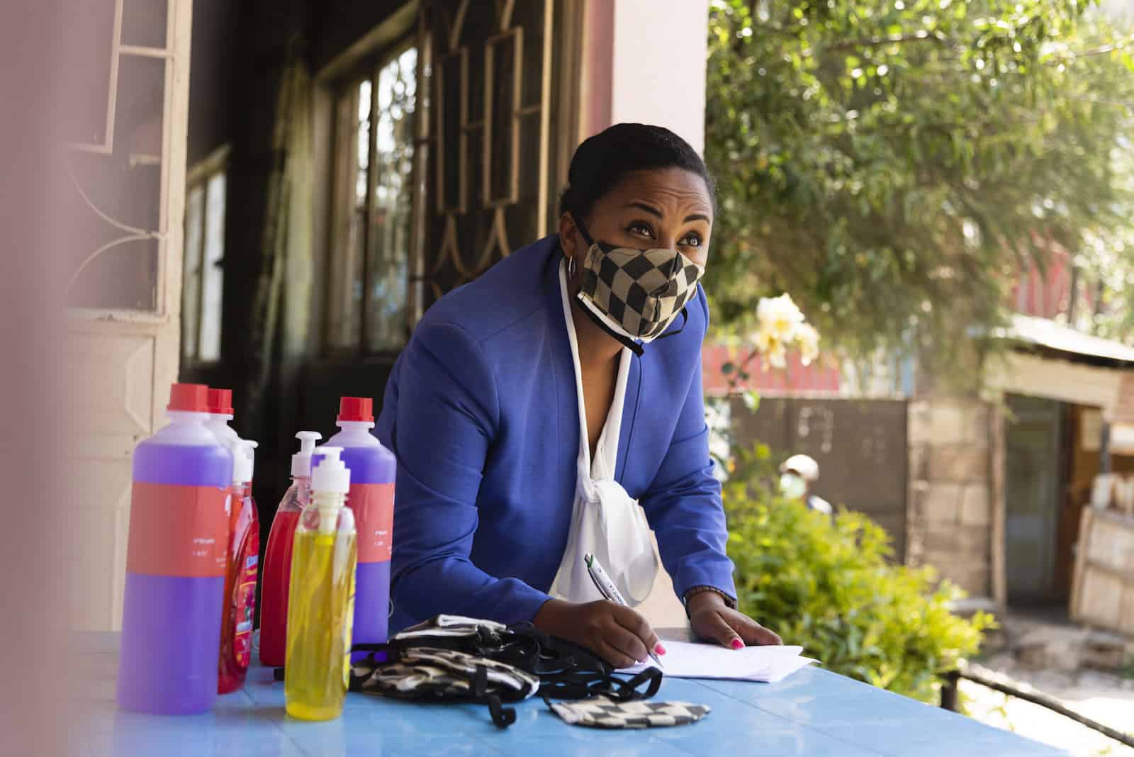 A woman wearing a mask stands at a desk with soap and masks