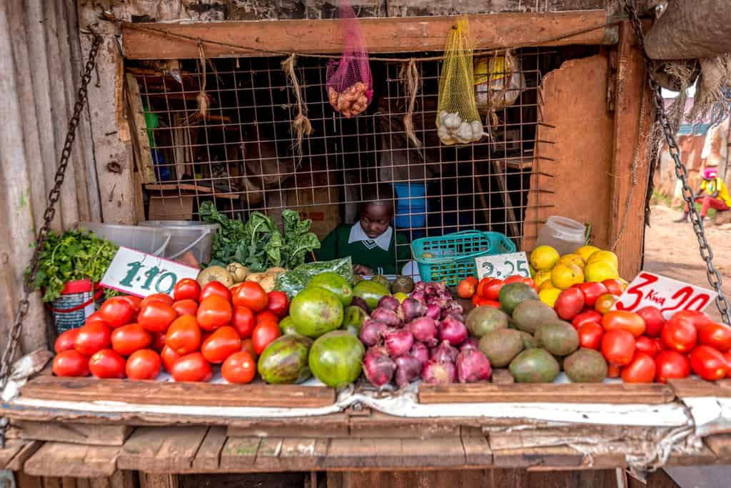 A child sitting behind a display of fruits at her grandmother’s shop.