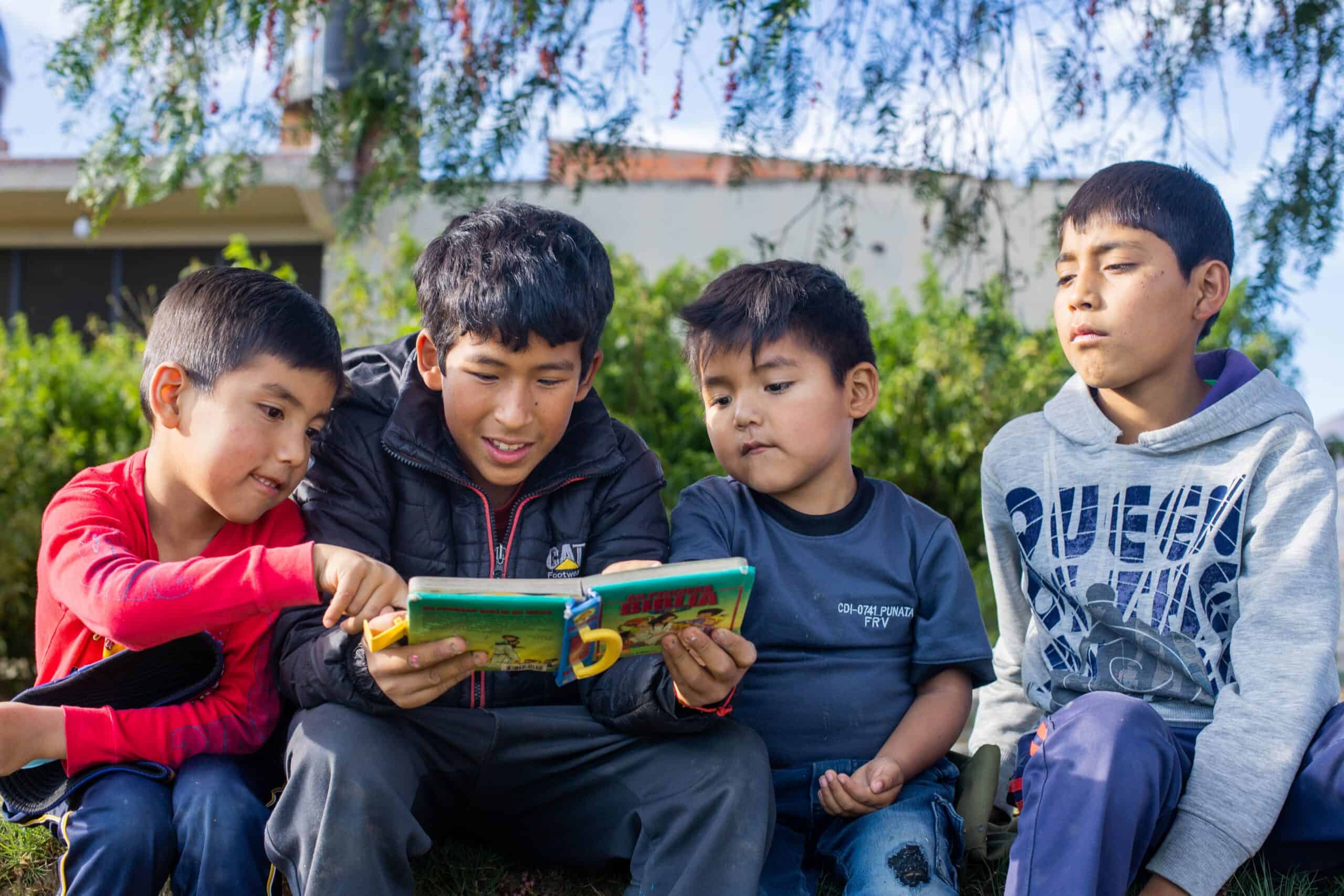 A group of four young boys sit outside and read the Bible together