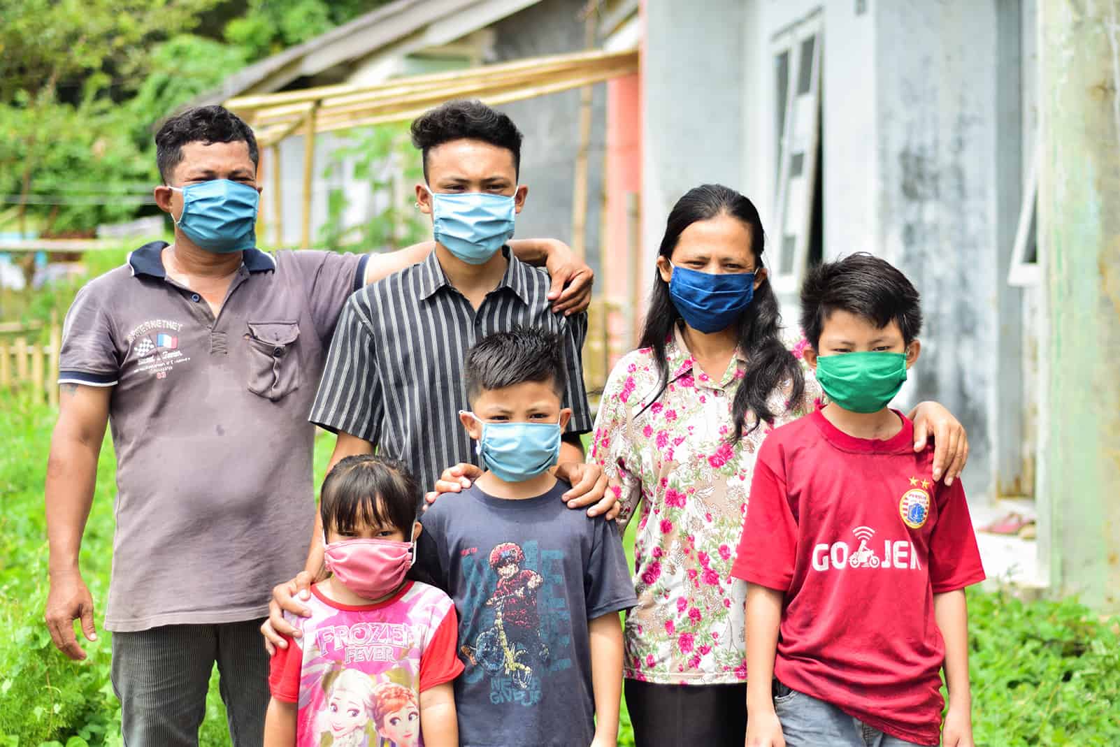 Julius and his family are standing outside of their house and are all wearing masks.