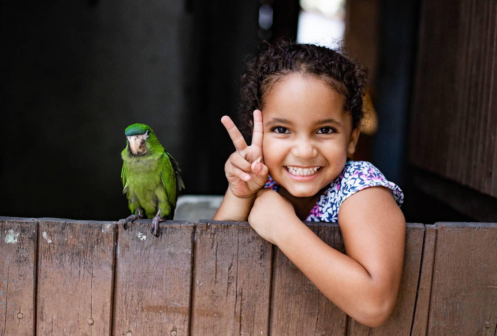 Maisa is at the back door to her house posing with her aunt's green parrot, Tico.