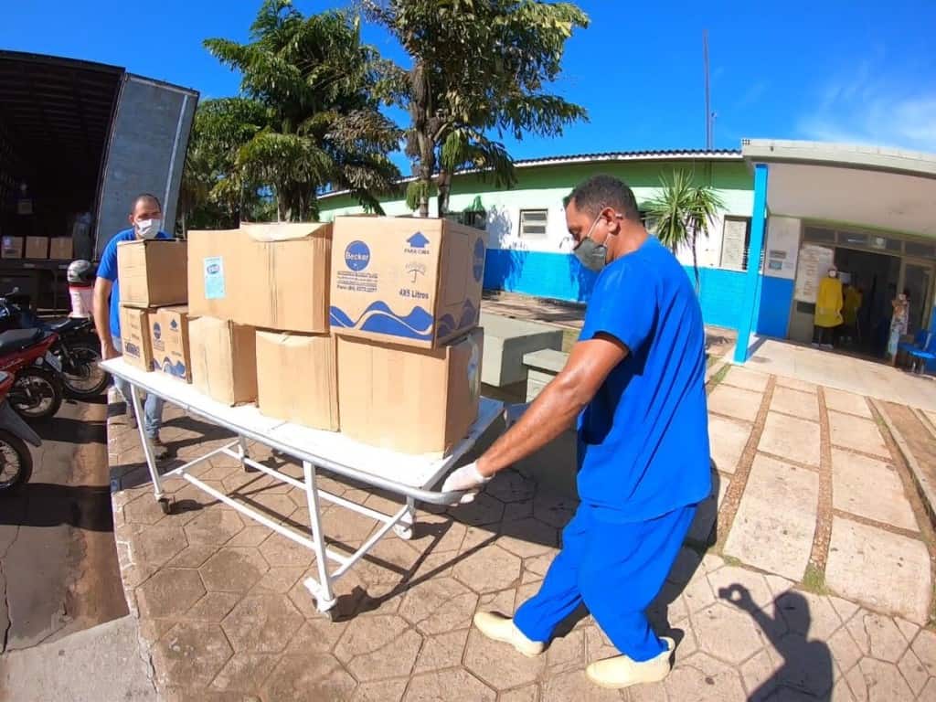 Two men wearing blue scrubs and masks wheeling a cart holding nine boxes of supplies