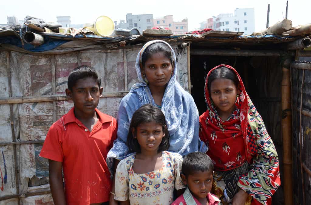 Family in the slums wearing traditional clothings. High rise buildings are in the background.