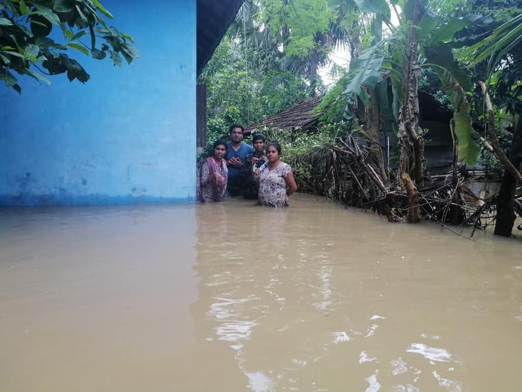 Four Compassion staff members are waist deep in water outside a blue building. They are going to meet Jenishtan and his family after the flood.