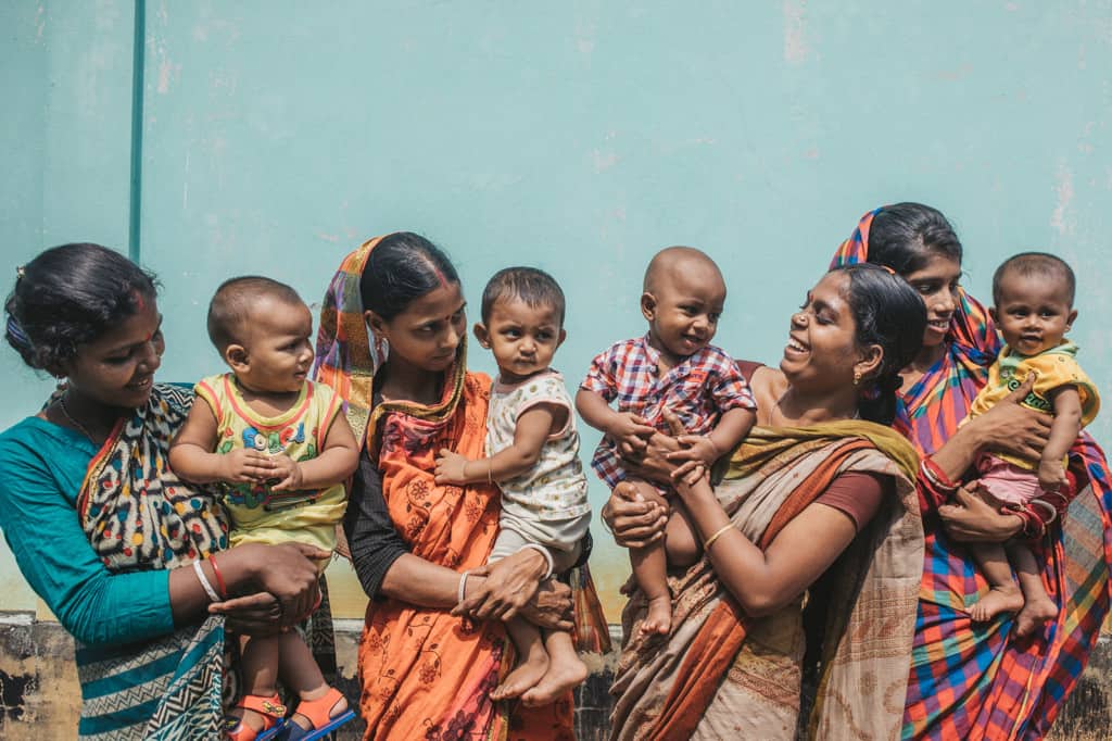 Several smiling and laughing mothers wearing traditional saaris holding their babies_