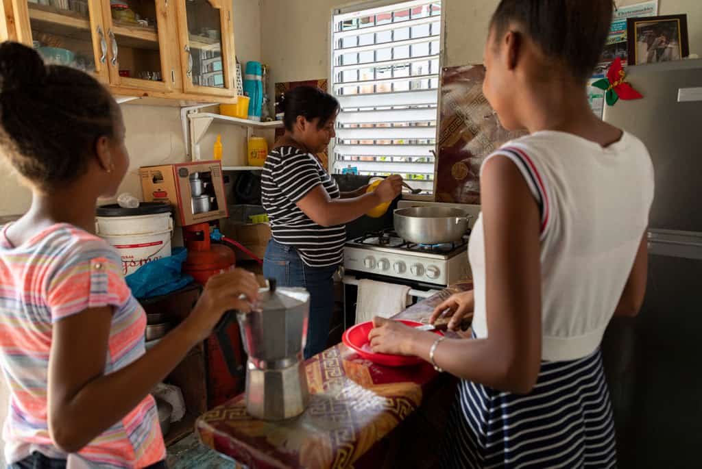 Mother and 2 daughters cooking together in a small kitchen.