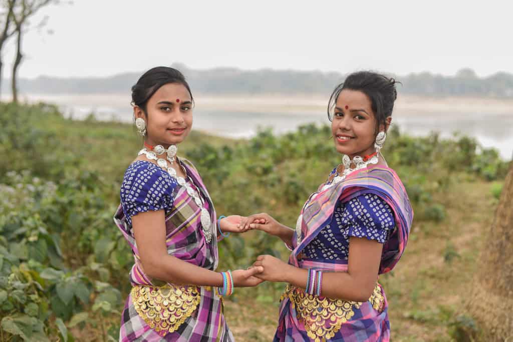 Two women standing in front of a small river and are dressed in colorful traditional clotihgin