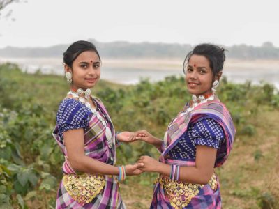 Two women standing in front of a small river and are dressed in colorful traditional clotihgin