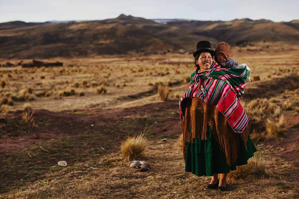 A local community leader wearing traditional dress in Titicani Turari poses for a photograph with her baby son.