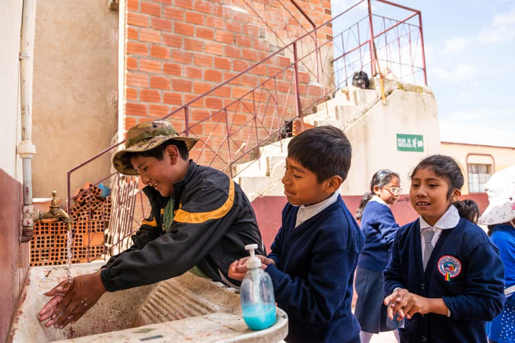 Children are standing at an outdoor sink washing their hands.