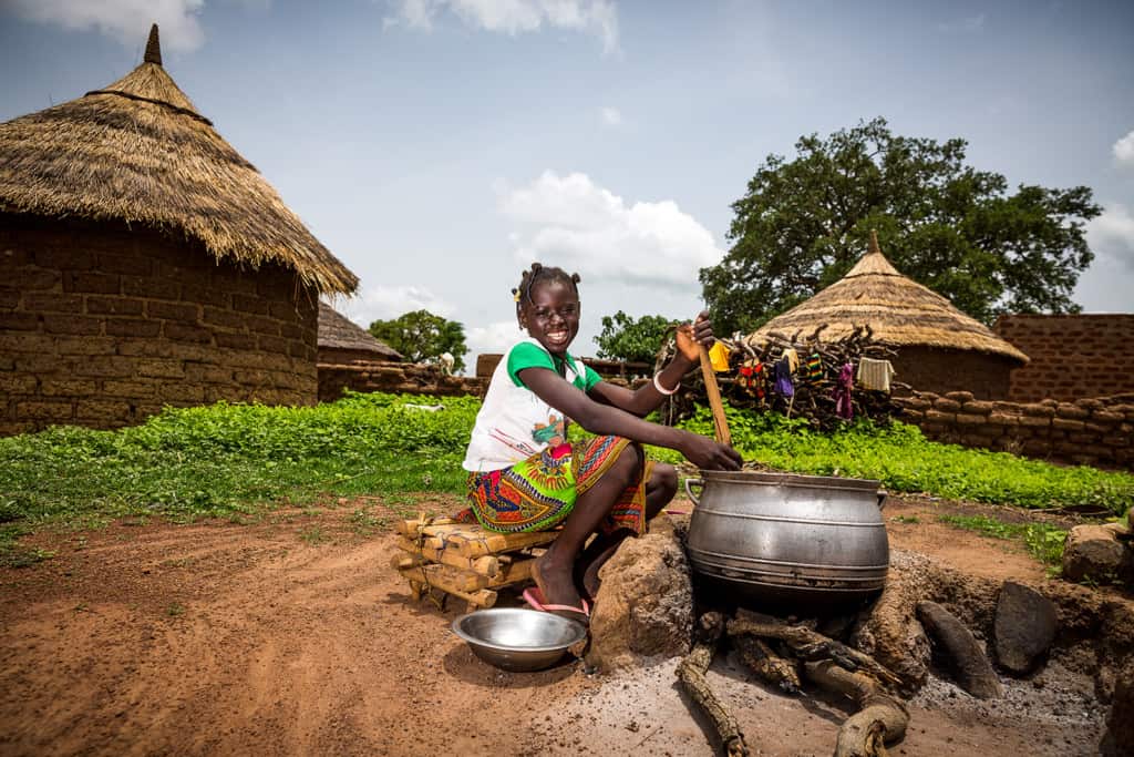 Girl sitting on a pile of firewood while stirring with her hands and meal preparation cooking making food.