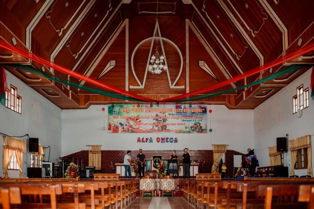 The inside of a church with wooden pews. There are people on the stage.