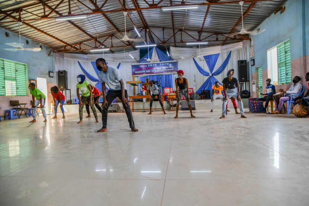 Large group dancing inside a compassion center all of the children are wearing face masks.